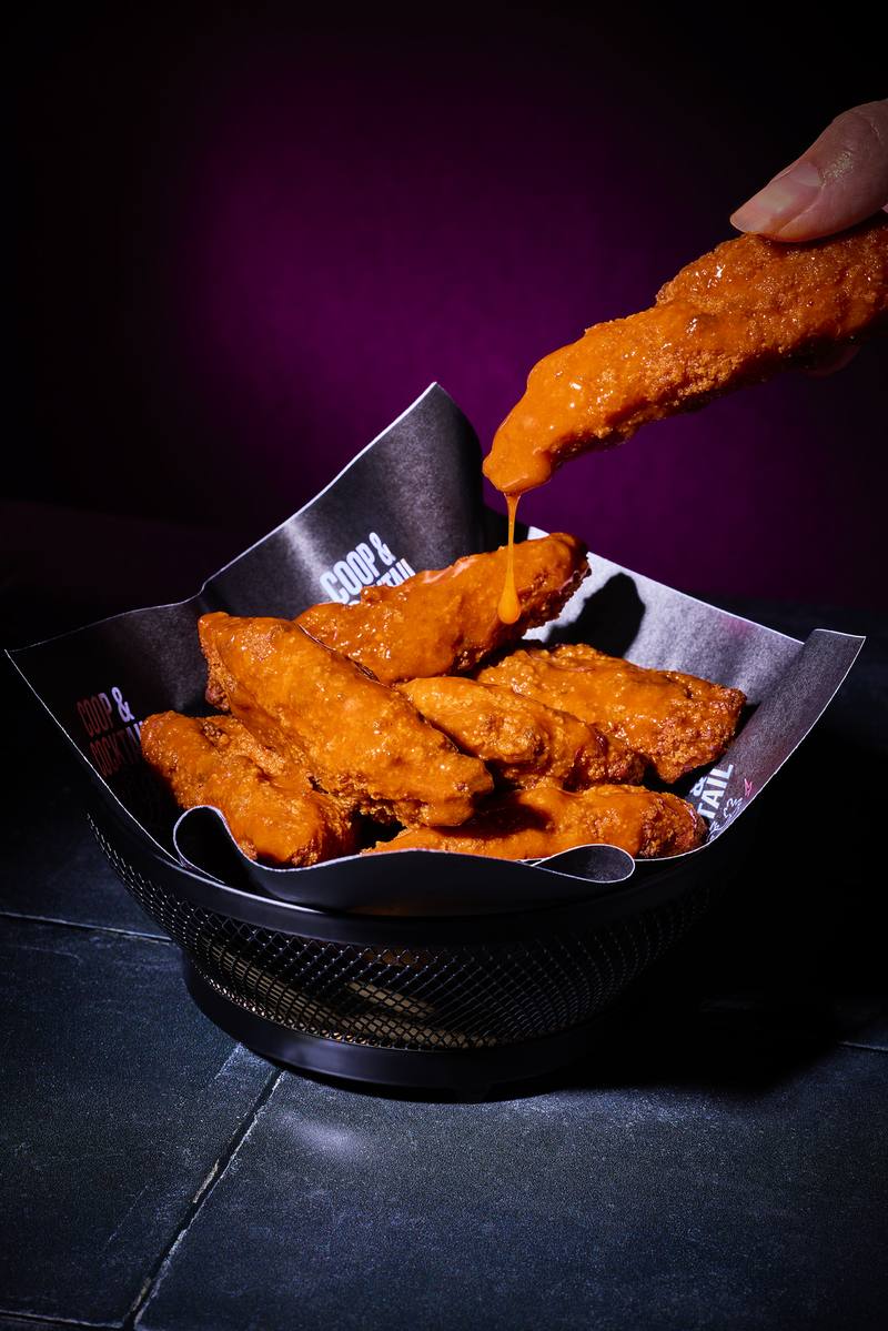 A hand lifting a buffalo tender with sauce dripping off the end